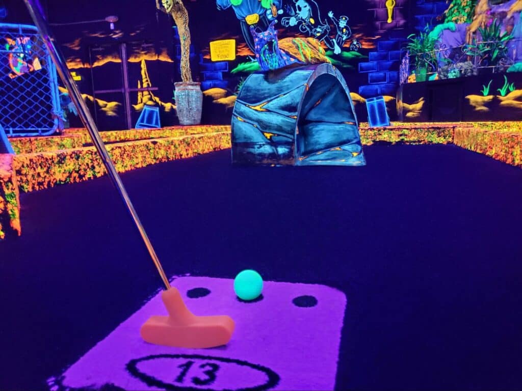 Monster Mini Golf Facilities 6 A putter and a neon golf ball at a glow-in-the-dark mini golf course location at monster mini golf.